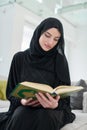 Portrait of young muslim woman reading Quran in modern home