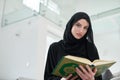 Portrait of young muslim woman reading Quran in modern home