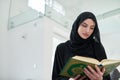 Portrait of young muslim woman reading Quran in modern home