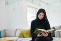 Portrait of young muslim woman reading Quran in modern home