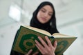 Portrait of young muslim woman reading Quran in modern home