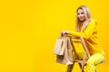 Portrait of young nice caucasian blonde woman with paper eco bags in yellow sportive suit, sitting on a wooden chair, isolated on Royalty Free Stock Photo