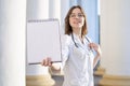 Portrait of a young nurse, medical university student standing with a phonendoscope and a blank sheet of paper, happy female