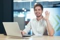Portrait of young office worker, man looking at camera and smiling waving hand greeting gesture, working on laptop businessman Royalty Free Stock Photo