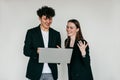 Portrait of young overemotive couple in black clothes. Young joyful man holding laptop near cheery woman shaking hands.