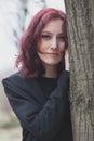 Portrait of young pale woman lean on tree winter day in park