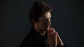 Portrait of a young pensive man on a dark background, looking to the side. Hands in prayer gesture. Royalty Free Stock Photo