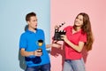 Portrait of young people, man with prize and woman with clapperboard isolated over blue-pink background. Movie time