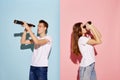 Portrait of young people, man and woman looking in binoculars isolated over blue-pink background. Waiting for vacation Royalty Free Stock Photo