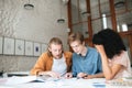 Young people working in office. Two boys with blond hair and girl with dark curly hair sitting and studying together in