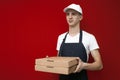 Portrait of a young pizza delivery man in uniform on a red background, a courier guy gives boxes of pizza Royalty Free Stock Photo