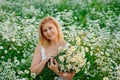 Portrait of a young, plump, beautiful woman resting on a chamomile field at sunset. A plus-size woman in a white sundress sits Royalty Free Stock Photo