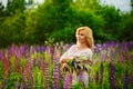 Portrait of a young plump blonde on a blooming field of lupines. A woman collects a bouquet of lilac-pink flowers in a meadow at Royalty Free Stock Photo