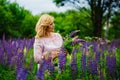 Portrait of a young plump blonde woman in a blooming field of lupines. A woman collects a bouquet of lilac-pink flowers in a Royalty Free Stock Photo