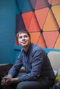 Portrait of young positive man sitting in the room with bright geometric wall looking up