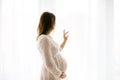 Portrait of young pregnant attractive woman, standing by the win