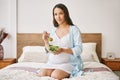 Portrait of young pregnant woman in pajama eating a fresh salad sitting in bed Royalty Free Stock Photo