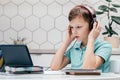 Portrait of young preteen boy covering headphones with hands, looking at screen of tablet, listening to online lesson. Royalty Free Stock Photo