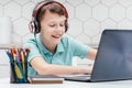 Portrait of preteen boy wearing headphones, sitting in front of laptop, typing, chatting, messaging, doing homework. Royalty Free Stock Photo