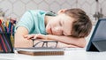 Portrait of young preteen tired boy lying sleeping on hands on desk near notebooks, glasses, color pencils, tablet. Royalty Free Stock Photo