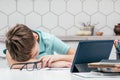 Portrait of young preteen weary pupil lying sleeping on hand on desk near notebooks, glasses, color pencils, tablet.