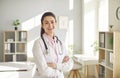 Portrait of a young pretty brunette female doctor in white medical uniform standing in her office. Royalty Free Stock Photo