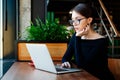 Portrait of young pretty business woman in glasses sitting on cafe and using laptop Royalty Free Stock Photo