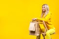 Portrait of young Pretty caucasian blonde woman with paper eco bags in yellow sportive suit, sitting on wooden chair, isolated on Royalty Free Stock Photo