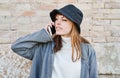 Portrait young pretty Caucasian girl, dressed in a gray jacket, a white sweater and a hat, talking on the mobile phone Royalty Free Stock Photo