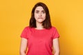 Portrait of young pretty emotional woman on yellow background, bites her lip, looks at camera with scared facial expression,