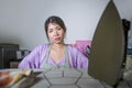 Portrait of young pretty frustrated and stressed Asian Korean woman working at home kitchen ironing clothes desperate and overwhel