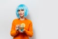 Portrait of young pretty girl with blue wig, holding glass mug with juice and piece of lemon. Wearing orange sweater.