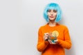 Portrait of young pretty girl with blue wig, holding glass mug with juice and piece of lemon. Wearing orange sweater.