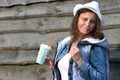 Portrait of young pretty girl in cowboy hat with milkshake in hand. Attractive woman in jeans jacket against wooden wall Royalty Free Stock Photo