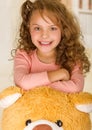 A portrait of a young pretty girl smiling and posing over her teddy bear head in a doctor office background Royalty Free Stock Photo