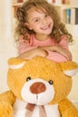 A portrait of a young pretty girl smiling and posing over her teddy bear s head in a doctor office background Royalty Free Stock Photo