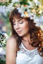 Portrait of a young pretty red-haired woman with closed eyes in a flowery garden, close-up