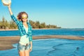 Portrait of young pretty smiling slim blond wearing mirrored heart shaped sunglasses waving a hat in her arm in a jump