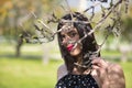 Portrait of young, pretty woman in a black dress with white polka dots, looking at the camera through the branches of a tree. Royalty Free Stock Photo