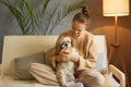 Portrait of young pretty woman in casual clothes hugging her beloved Pekingese dog sitting on the sofa in the living room of her Royalty Free Stock Photo