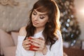 Portrait of young pretty woman with cup of tea in New year interior. Beautiful model girl in cozy sweater and knee socks Royalty Free Stock Photo