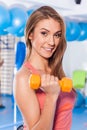 Portrait of a young pretty woman holding weights (dumbbell) and doing fitness indor. Crossfit hall. Gym shot.