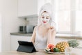 Portrait of young pretty woman with mud facial mask on her face and hair wrapped in towel, sitting at the table with Royalty Free Stock Photo