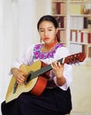 Portrait of young pretty woman wearing beautiful traditional andean clothing, sitting down with acoustic guitar playing Royalty Free Stock Photo