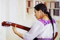 Portrait of young pretty woman wearing beautiful traditional andean clothing, sitting down with acoustic guitar playing Royalty Free Stock Photo