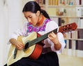Portrait of young pretty woman wearing beautiful traditional andean clothing, sitting down with acoustic guitar playing Royalty Free Stock Photo
