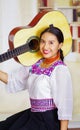 Portrait of young pretty woman wearing beautiful traditional andean clothing, sitting down holding acoustic guitar up Royalty Free Stock Photo