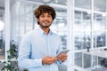 Portrait of young programmer with tablet computer inside office, hispanic man with curly hair smiling and looking at Royalty Free Stock Photo