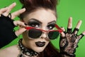 Portrait of young punk woman wearing sunglasses over green background