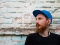 Portrait of young red bearded man in black t-shirt and snapback in rock style on urban background listening to music Royalty Free Stock Photo